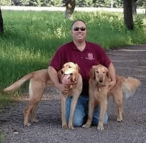 Dr. James Van Stone DVM kneeling outdoors with two golden retriever dogs